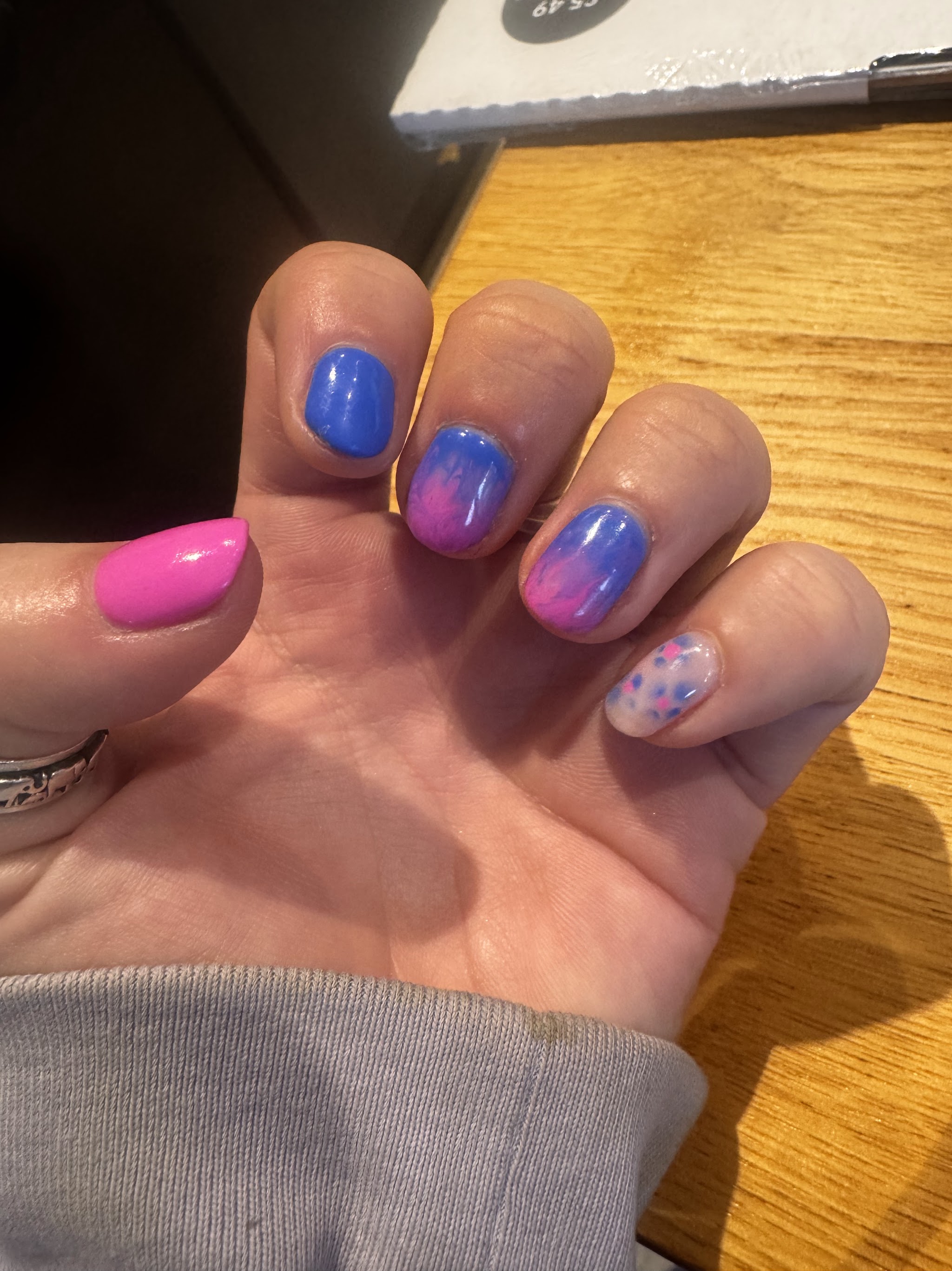 Short gel nails in pink and blue ombre with a speckled accent nail