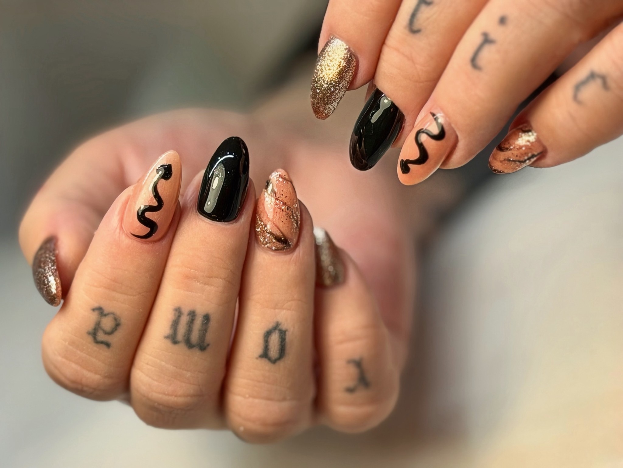 Almond nails mixing black, nude, glitter and hand-painted swirl nail art